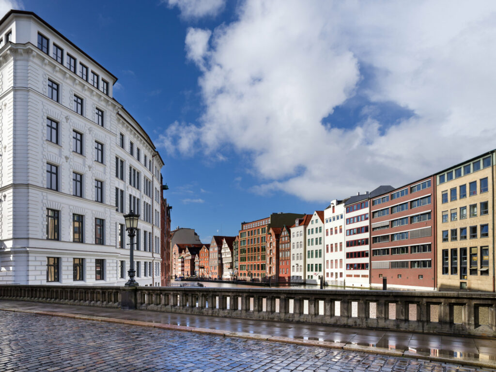 Eine Brücke mit Kopfsteinpflaster, im Hintergrund eine Reihe von Häusern entlang des Flusses.