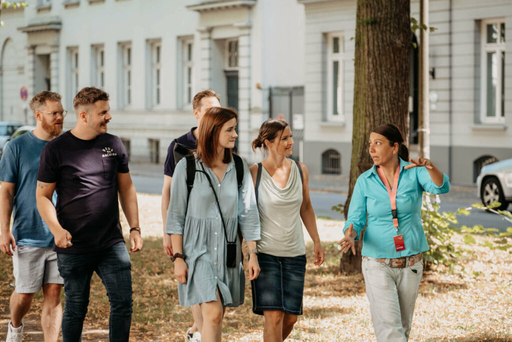 Eine Gruppe von Menschen, angeführt von einer Frau, die vorangeht und etwas erzählt.
