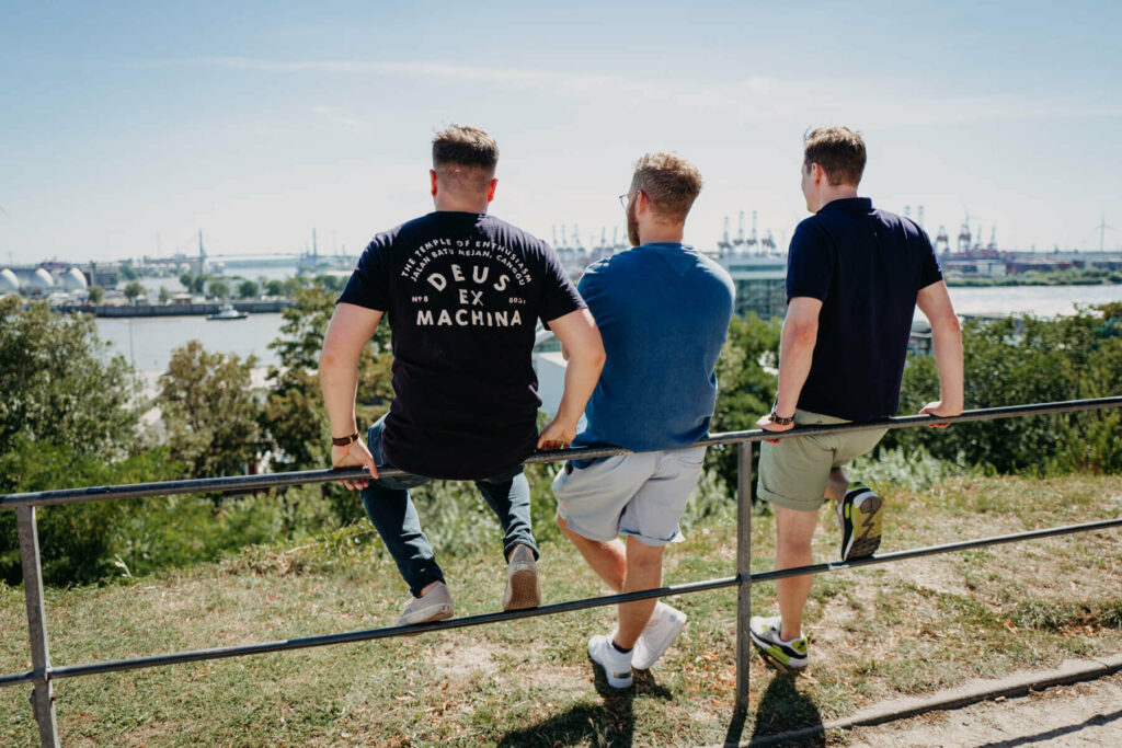 Drei Männer lehnen lässig an einem Geländer und genießen den Blick auf die Elbe.