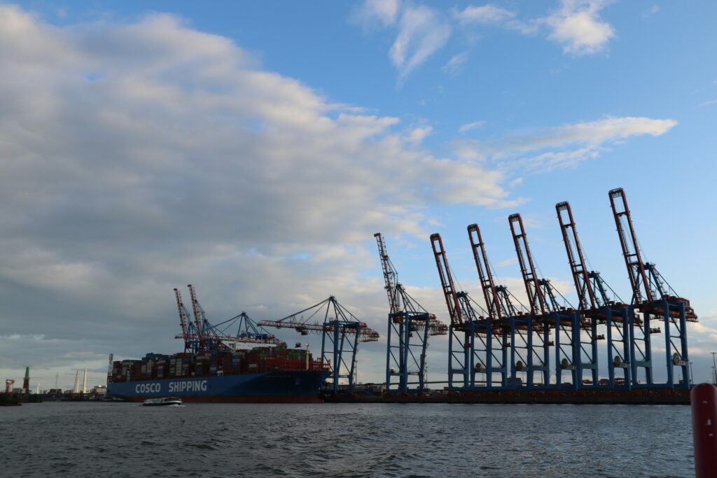 Ein großes Schiff fährt auf der Elbe an mehreren Hafenkränen vorbei.
